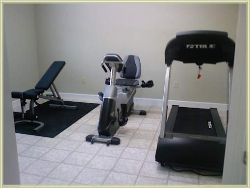 A black treadmill with the word TRUE on it sits in a room with a mirror and a weight bench.