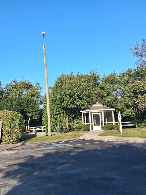 A gazebo is located in a park with a tall pole and a bench.
