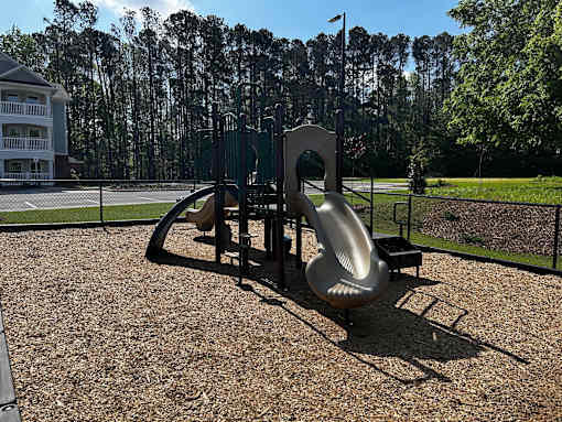 A playground with a slide and a green fence.