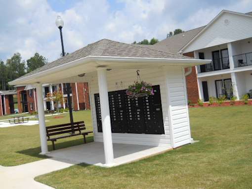 A small white pavilion with a black board and bench in front of a brick building.