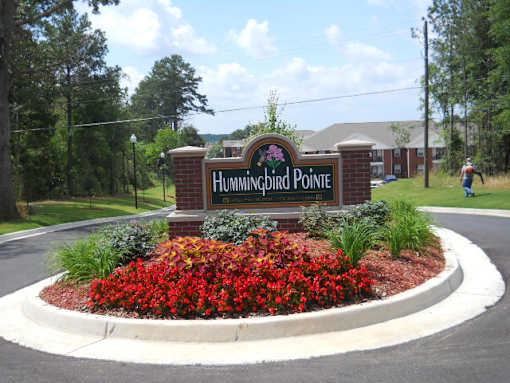 A sign that says Hummingbird Pointe in front of a flower bed.