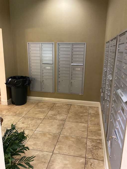 A room with a wall of mailboxes and a trash can.