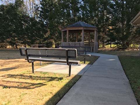 A gazebo is behind a bench on a concrete walkway.