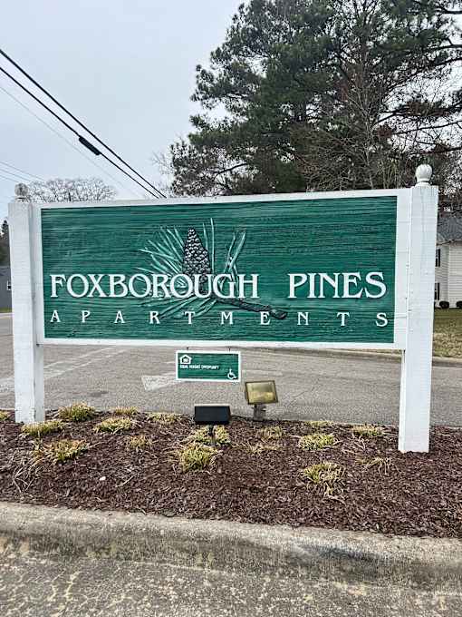 A sign for Foxborough Pines Apartments stands on a sidewalk.