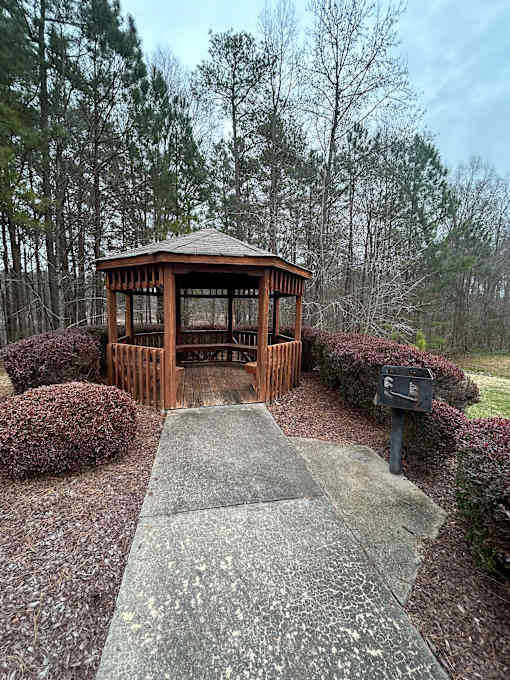 A wooden structure with a glass window is surrounded by a stone wall and trees.