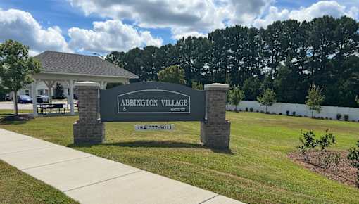 A sign for Abbington Village stands in front of a building and trees.