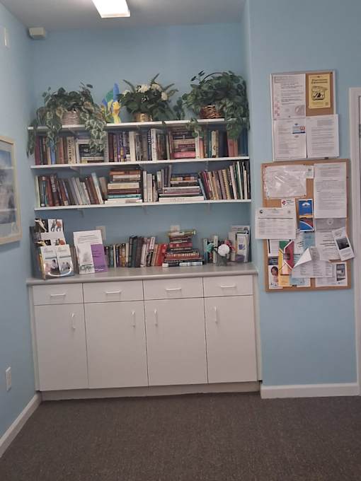 A room with a blue wall and a white cabinet under a shelf with books and a bulletin board on the wall.