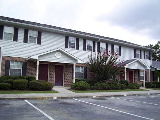 A grey building with a red door and a tree in front.