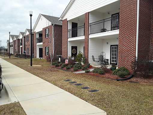 A row of red and white townhouses with a sidewalk in front.