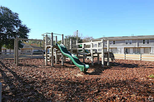A playground with a green slide and brown leaves on the ground.