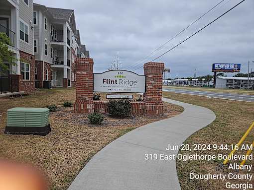 A sign for Flint Ridge Apartments is displayed in front of a brick wall.