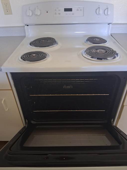 A white stove top with four burners and an open oven below it.