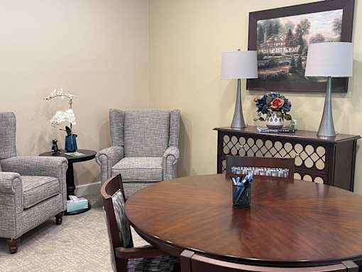 A living room with a grey couch, a grey chair, a wooden table and a painting on the wall.