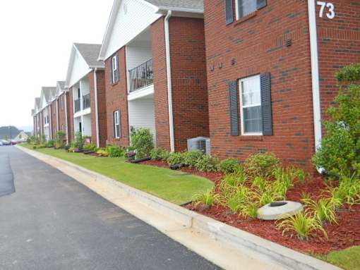 A row of red brick apartment buildings with green bushes in front.