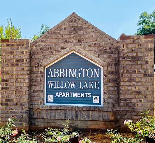 A brick wall with a sign that says Abbington Willow Lake Apartments.