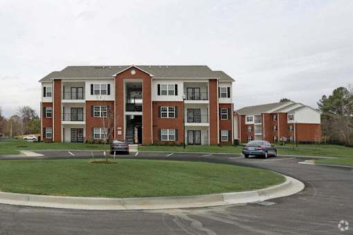 A large red brick apartment building with a parking lot in front.