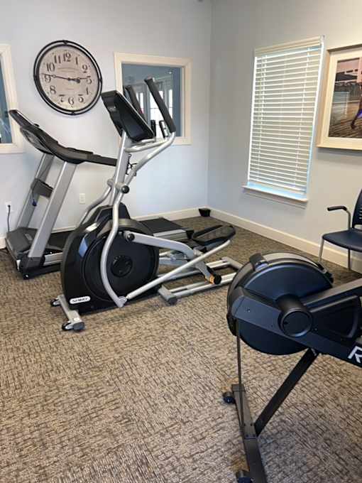A gym room with a treadmill, a stationary bike, and a clock on the wall.