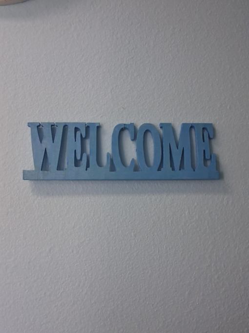 A blue sign that says "welcome" is mounted on a white wall.