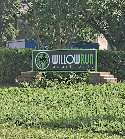 A sign for Willow Run Apartments is in front of a hedge.