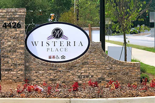 A sign for Wisteria Place with a brick wall and flowers.