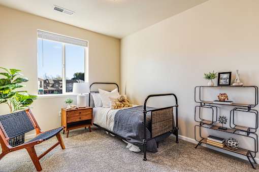 A bedroom with a bed, chair, and shelf.