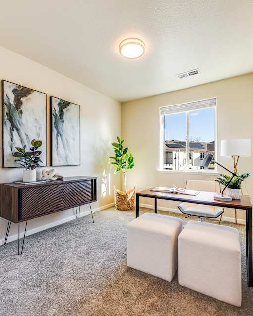 A room with a desk, chair, and two potted plants.