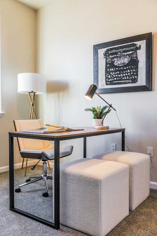 A black and white picture of a typewriter is hanging on a wall above a desk with a chair and a lamp.