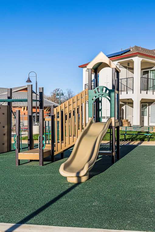 A playground with a slide and a building in the background.