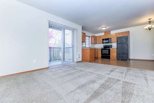 A spacious living room with a large rug, a television, and a kitchenette in the background.