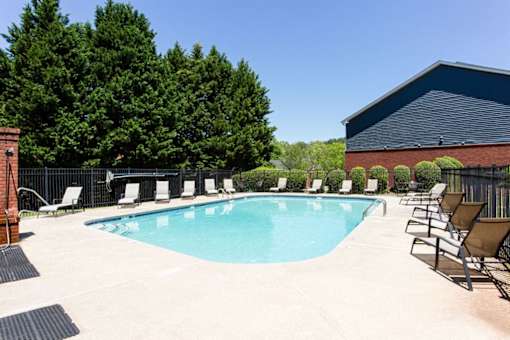 A pool surrounded by trees and chairs at Ballantyne Commons of Stockbridge Apartments, Stockbridge, GA