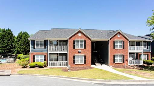 A red brick apartment building with a green lawn in front at Ballantyne Commons of Stockbridge Apartments, Stockbridge, Georgia