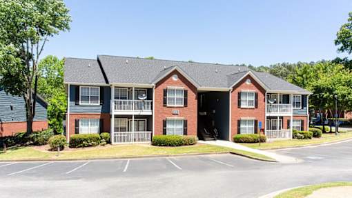 A red brick apartment building with a parking lot in front at Ballantyne Commons of Stockbridge Apartments, GA, 30281