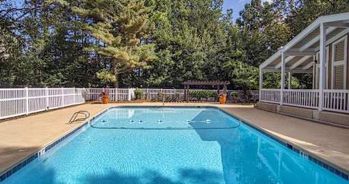 A blue swimming pool surrounded by a white fence and trees at The Madison Apartments and Townhomes, Lawrenceville, 30044