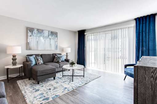 A living room with a grey couch, a blue rug, and a painting on the wall at Barcelo at East Cobb Apartments, Marietta, GA, 30067