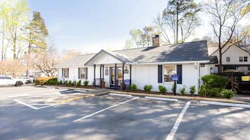 A white building with a black roof is surrounded by a parking lot at Barcelo at East Cobb Apartments, Marietta, GA