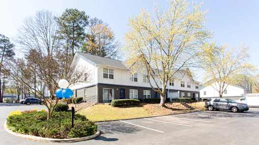 A white building with a grey roof and a blue sign in front of it at Barcelo at East Cobb Apartments, Georgia