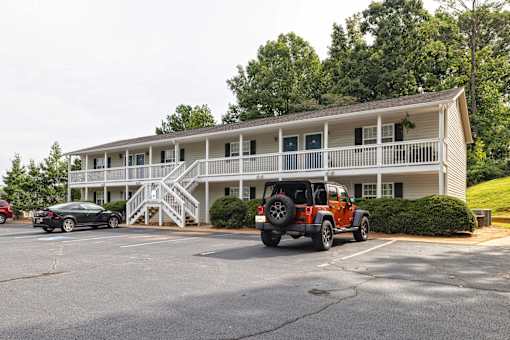 A red car is parked in front of a white building with a black car parked behind it at Overlook Club Apartments, Cummings