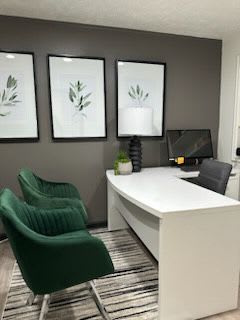 A white desk with a black chair and three framed pictures on the wall.