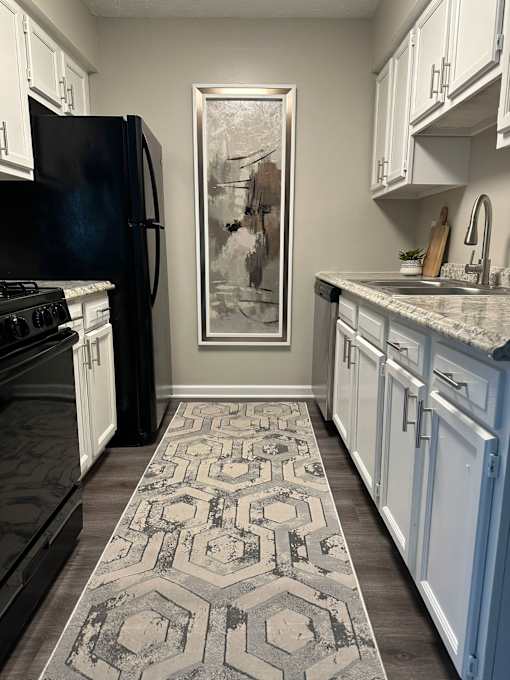 A kitchen with a black fridge and a rug on the floor.