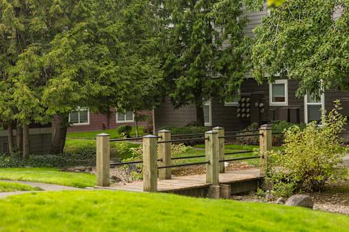 A wooden bridge over a grassy area with a house in the background.