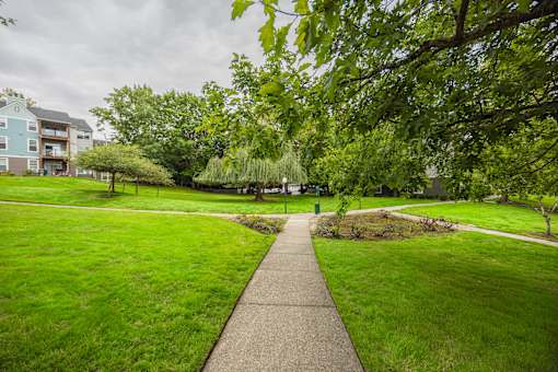 A pathway leads through a grassy area with trees and a building in the background.