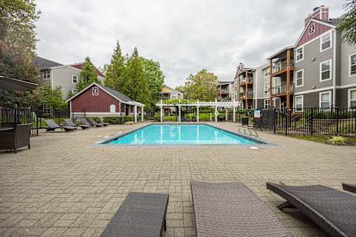 A pool surrounded by a black fence and a red barn.