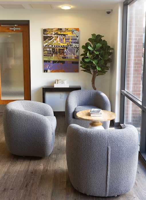 Three grey chairs are arranged around a small table in a room with a large window.