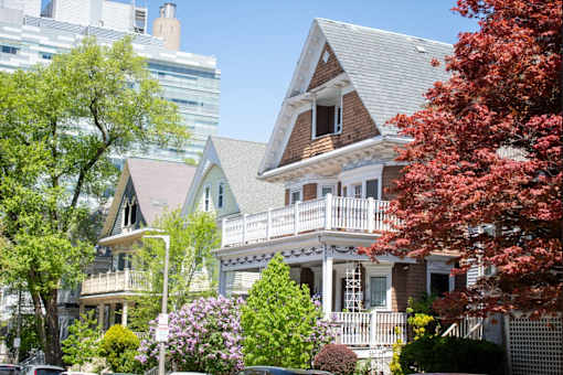 a row of houses with trees and a skyscraper in the background