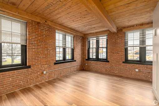 A room with wooden floors and brick walls has three windows.