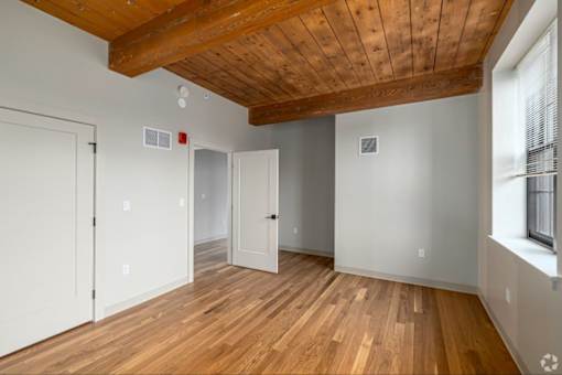 A room with wooden floors and a wooden ceiling with a white door on the left and a white door in the middle.