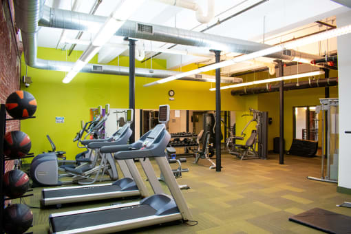 a gym with cardio equipment and a yellow wall