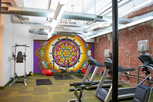 a gym with exercise equipment and a colorful mural on the wall