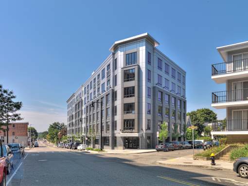 A street view of a modern multi-story building with cars parked on the side of the road.