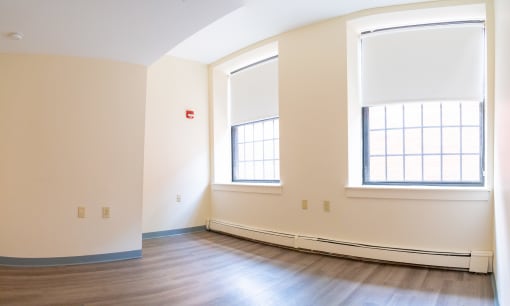 an empty room with two windows and hardwood floors